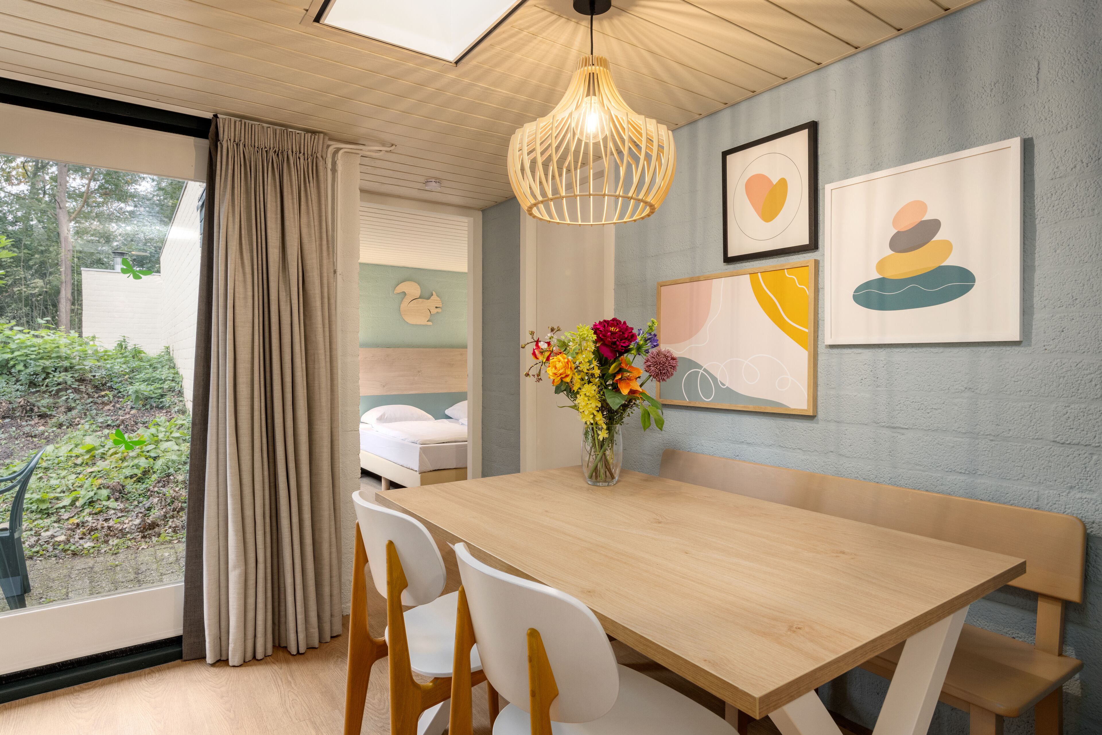 Een eetruimte met een houten tafel, witte stoelen, een hanglamp en kunst aan de muur.