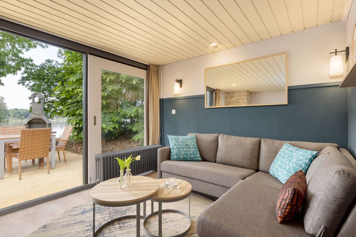 A modern living room with a sofa, two round tables, and a large window overlooking a patio area.