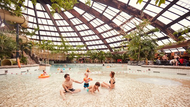 Una piscina interior con techos altos y paneles de vidrio, rodeada de diversas toboganes y piscinas.