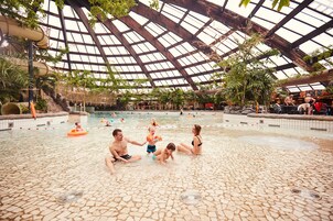 Una piscina interior con techos altos y paneles de vidrio, rodeada de diversas toboganes y piscinas.