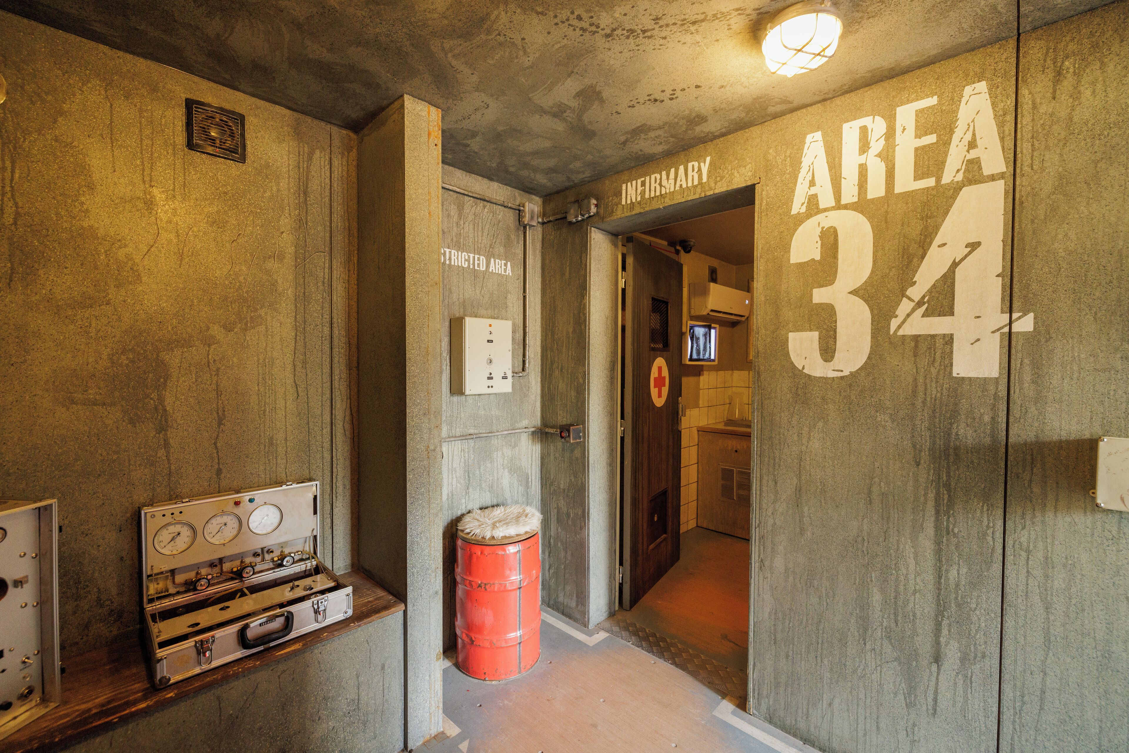 A hallway with a sign reading "Area 34" and "Restricted Area," a red barrel, and a vintage suitcase with dials.