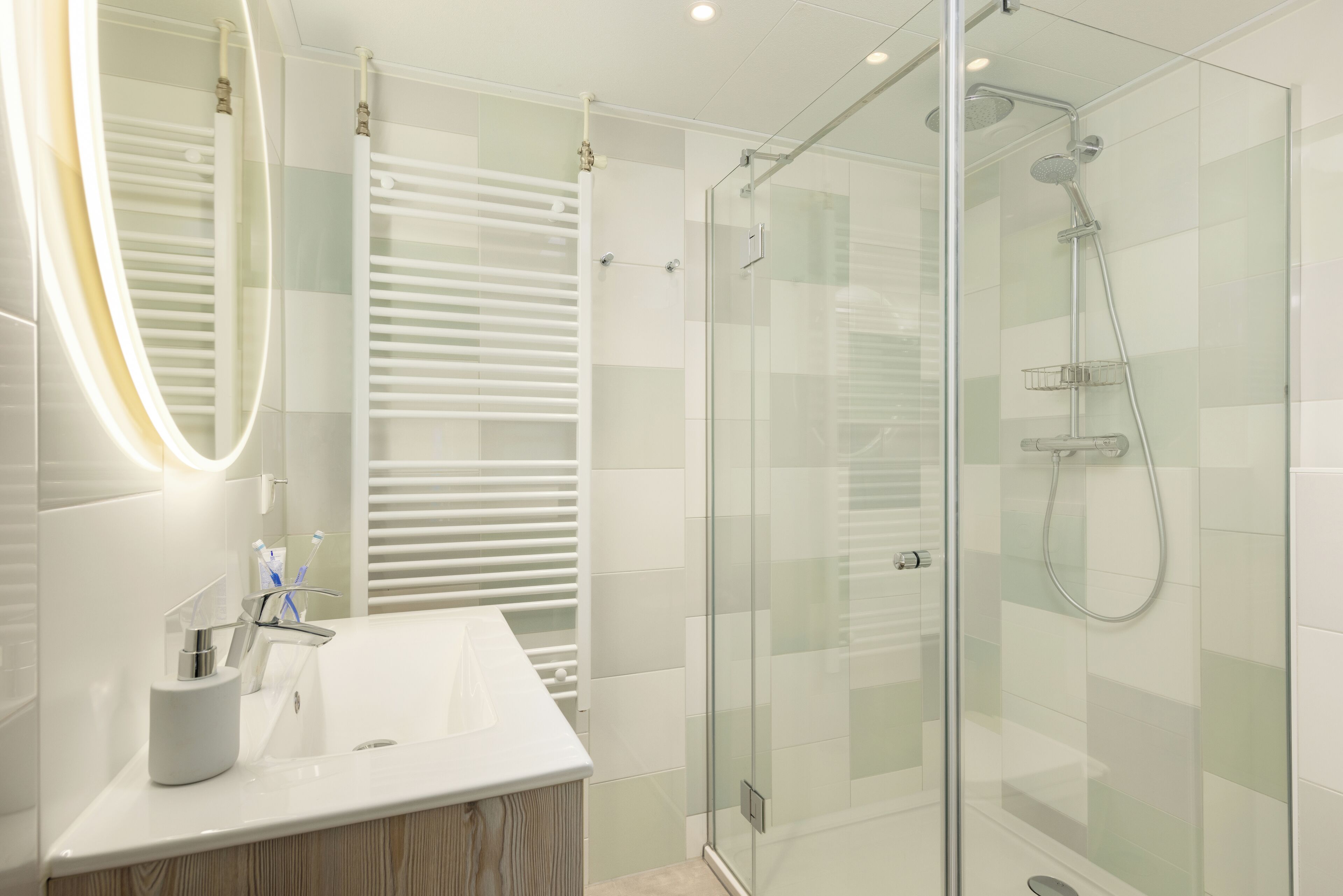 Une salle de bain moderne avec une douche à parois de verre, un lavabo blanc avec un miroir et un porte-serviettes.