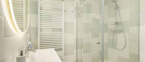 Une salle de bain moderne avec une douche à parois de verre, un lavabo blanc avec un miroir et un porte-serviettes.