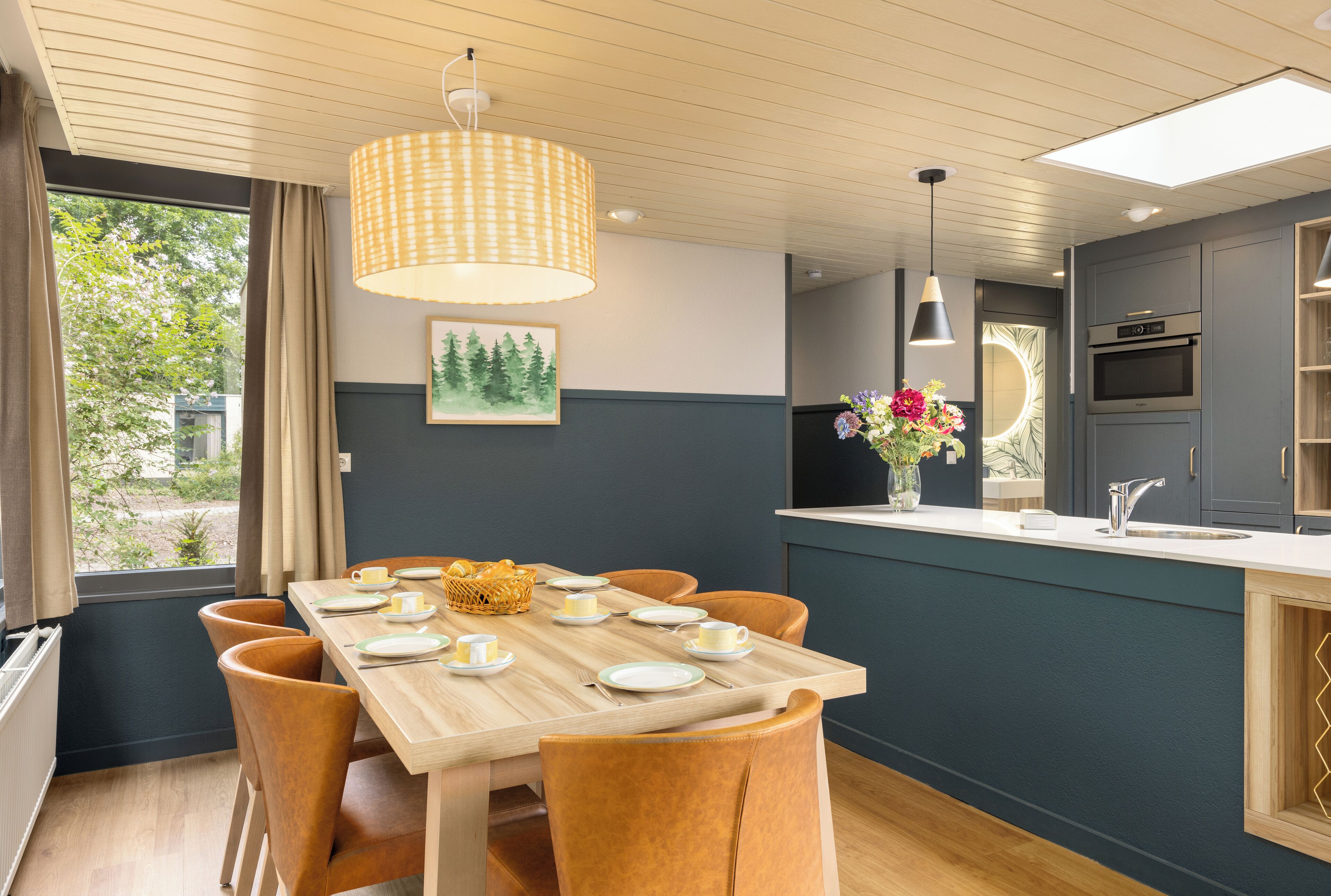 A modern kitchen with a wooden dining table set for four, a built-in oven, and a view of the outdoors.