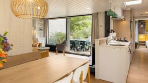 Una cocina moderna con una isla central, un área de comedor con mesa de madera y vistas al exterior a través de amplios ventanales.