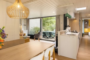 Una cocina moderna con una isla central, un área de comedor con mesa de madera y vistas al exterior a través de amplios ventanales.