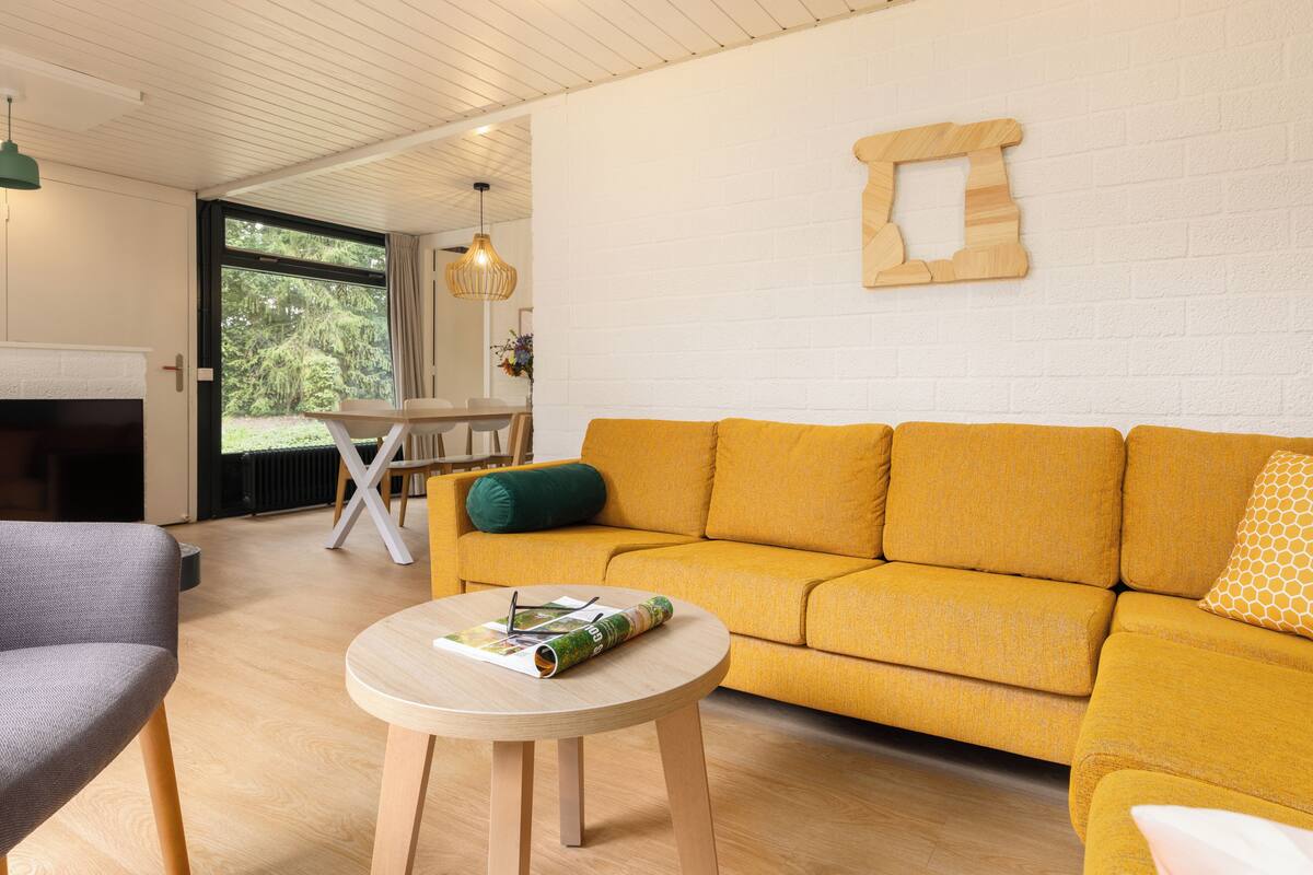 A modern living room with a yellow sofa, a round wooden table, and a grey armchair.