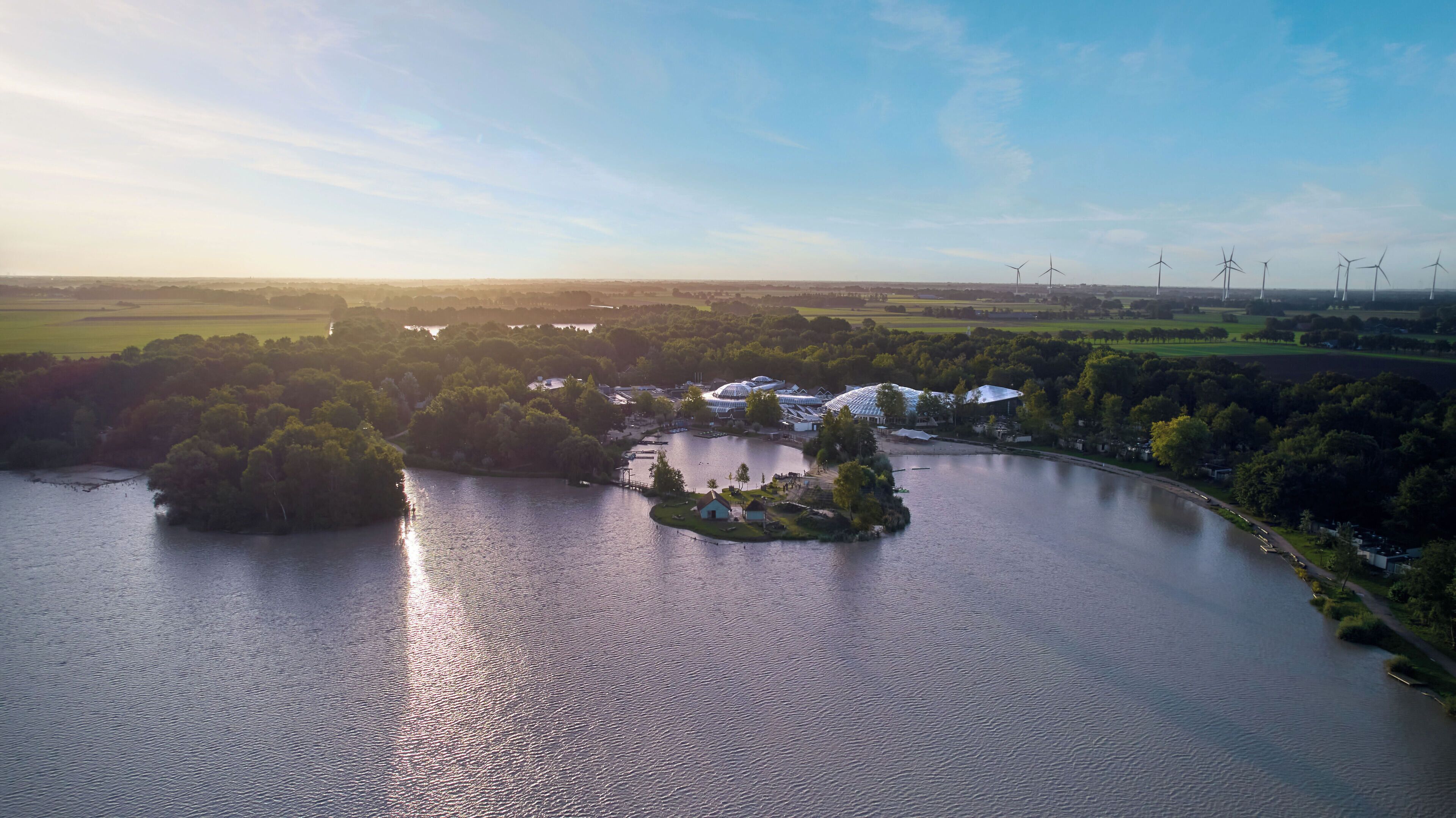 An aerial view of a lakeside property with a small island, surrounded by lush greenery and a clear sky.
