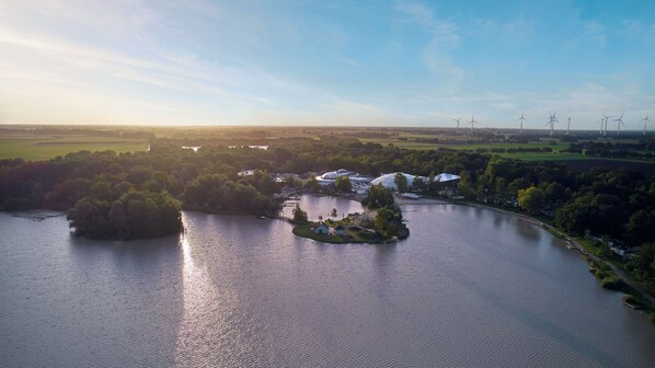 An aerial view of a lakeside property with a small island, surrounded by lush greenery and a clear sky.