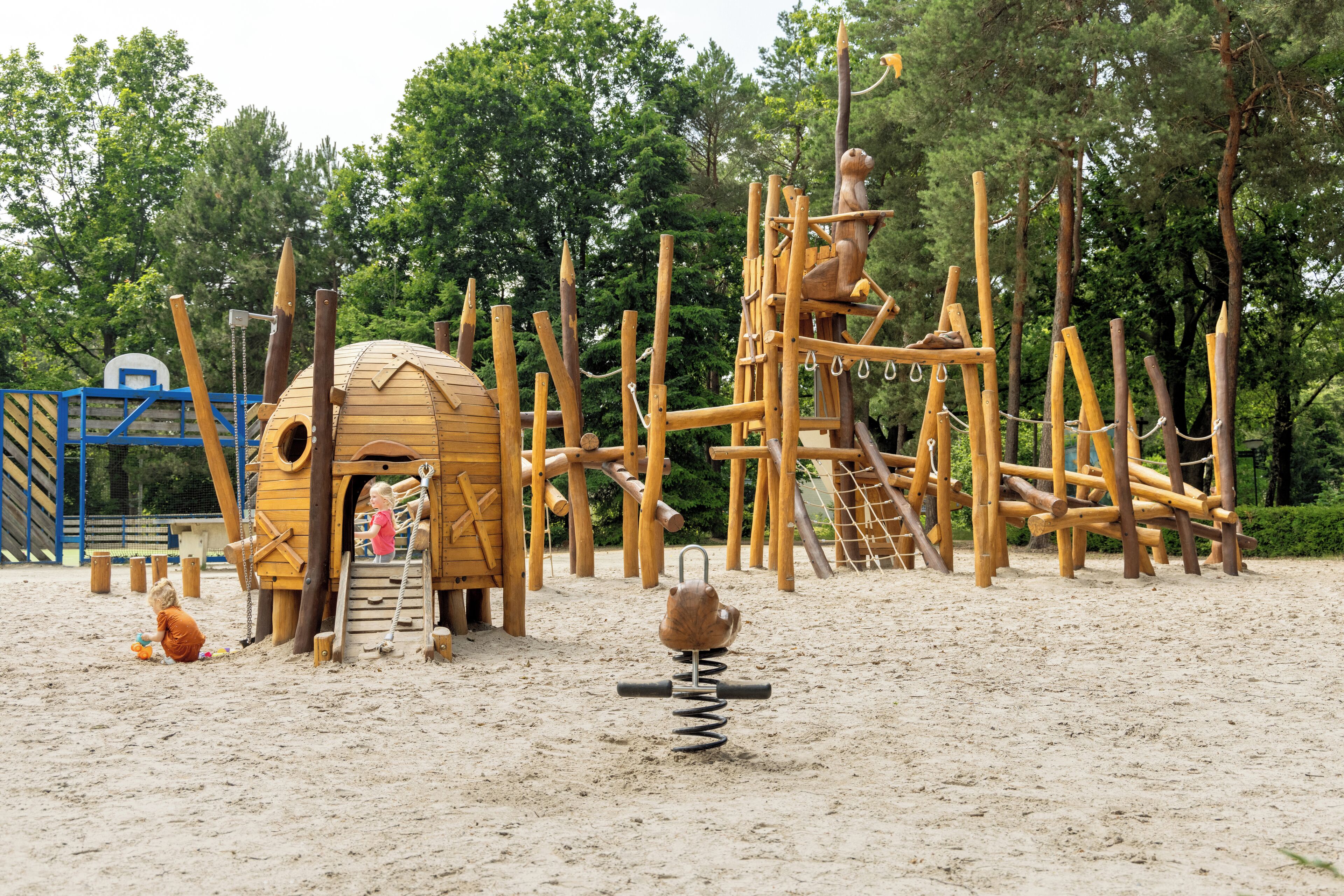 Een speeltuin met houten klimconstructies en een koepelvormig speelhuis.