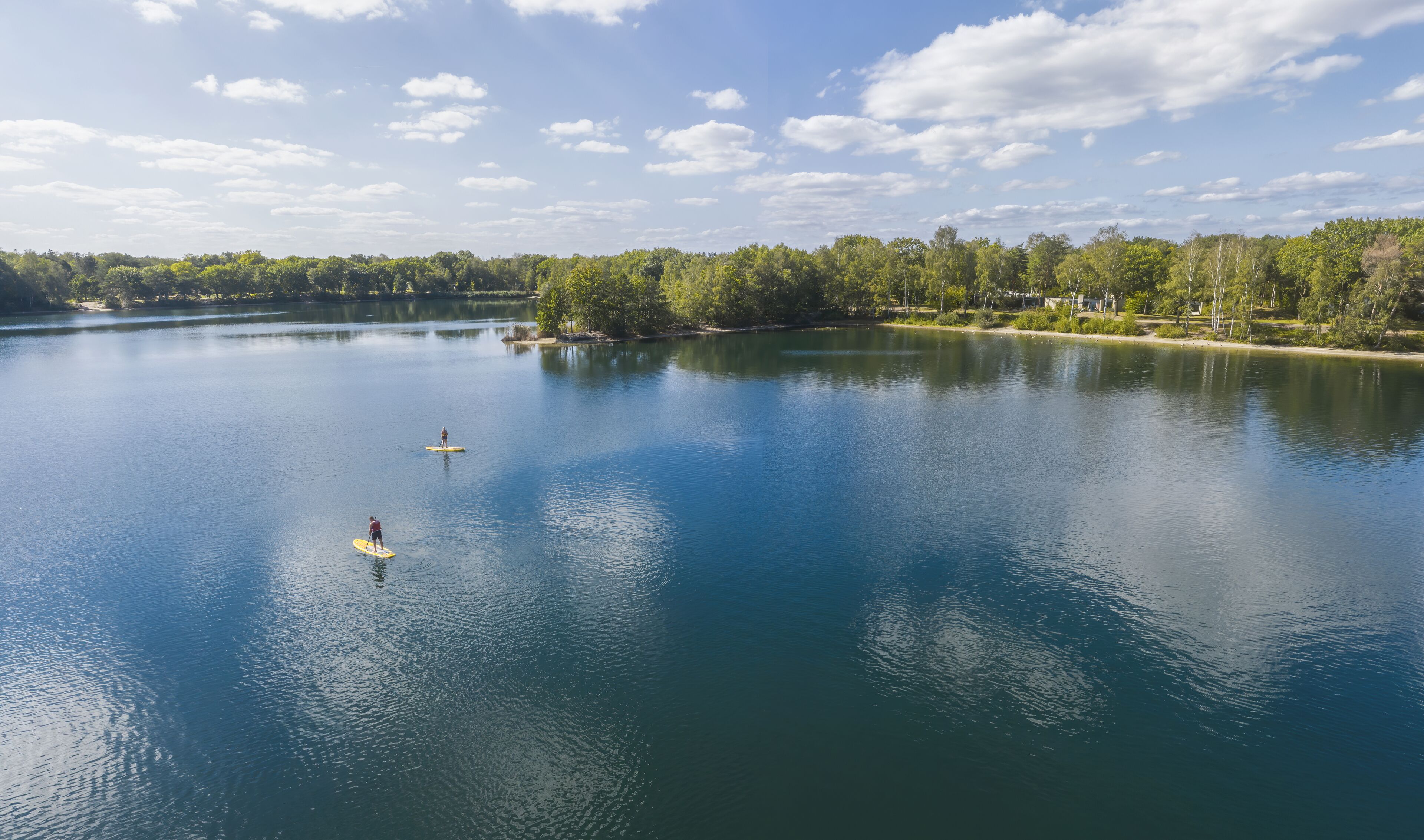 A calm lake with two paddleboards, surrounded by dense trees and a clear sky.