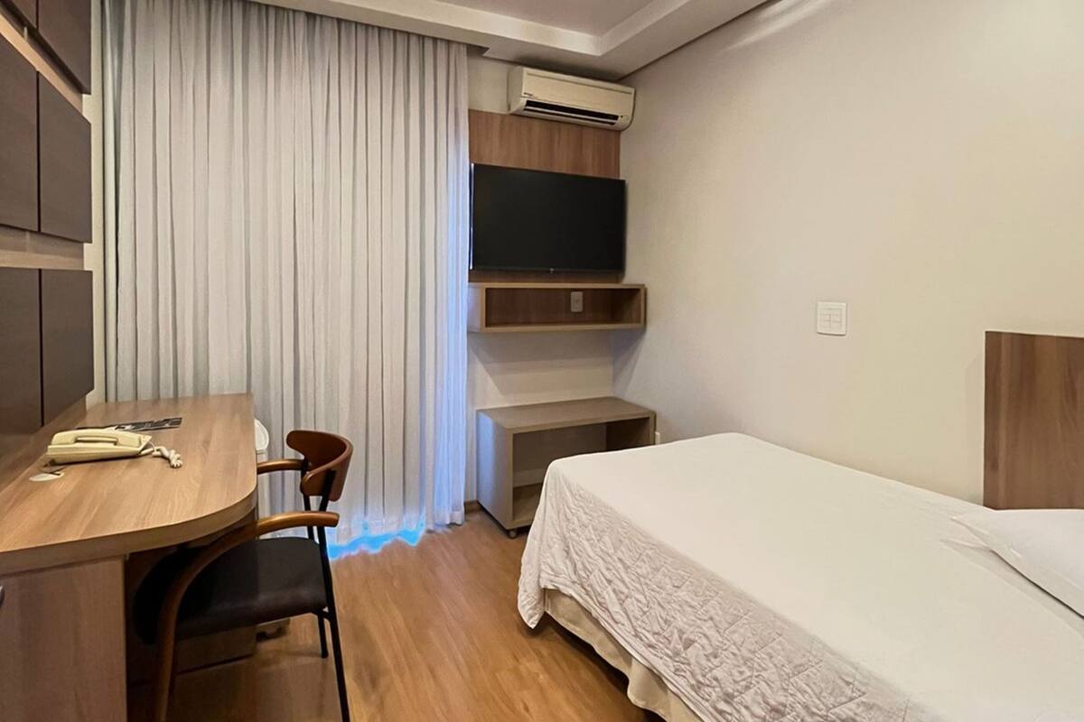 Una habitación de hotel moderna con un escritorio de madera, una cama con edredón blanco, un televisor de pantalla plana montado en la pared y un equipo de aire acondicionado.
