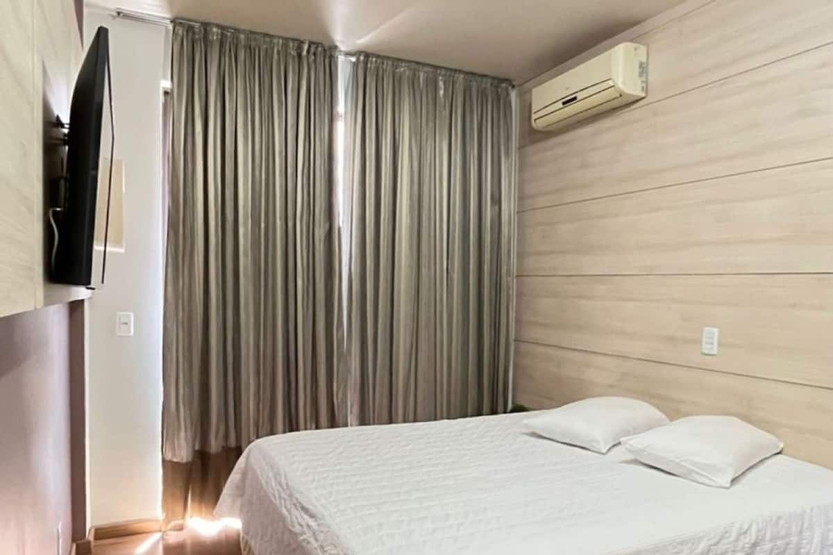 Un dormitorio con una cama, un televisor montado en la pared y un equipo de aire acondicionado.
