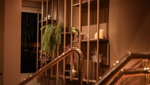 Un escalier avec des rampes en métal menant à un palier où se trouvent des étagères ornées d’objets décoratifs et de plantes.
