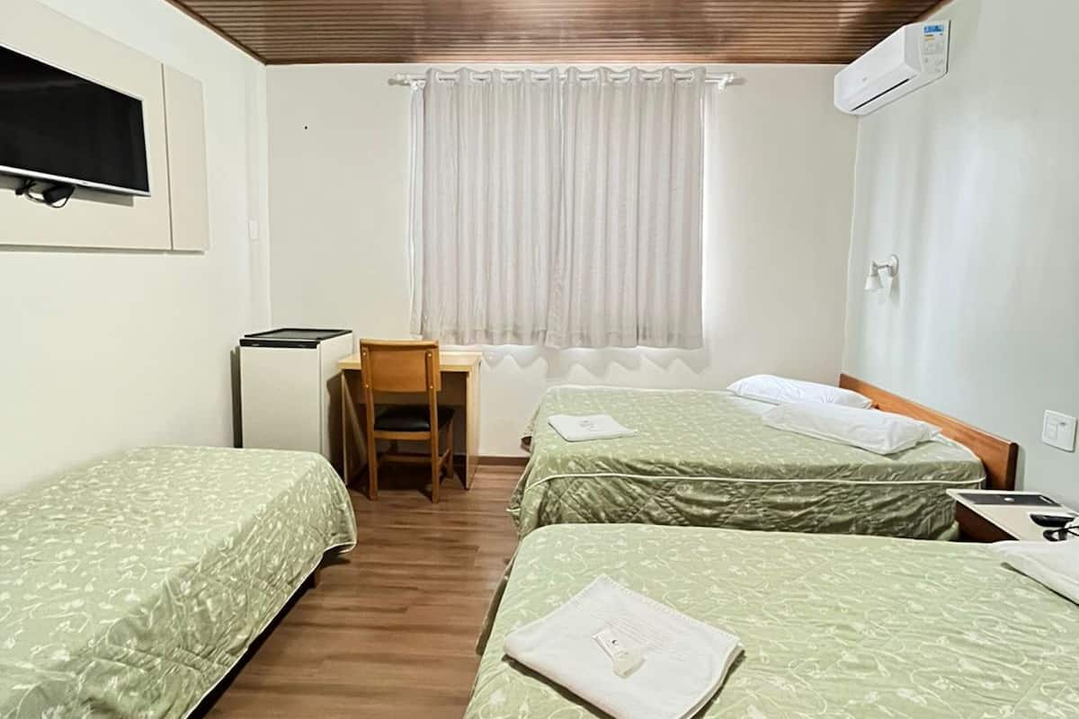 Una habitación con dos camas individuales, un escritorio con una silla, un televisor montado en la pared y un aire acondicionado.