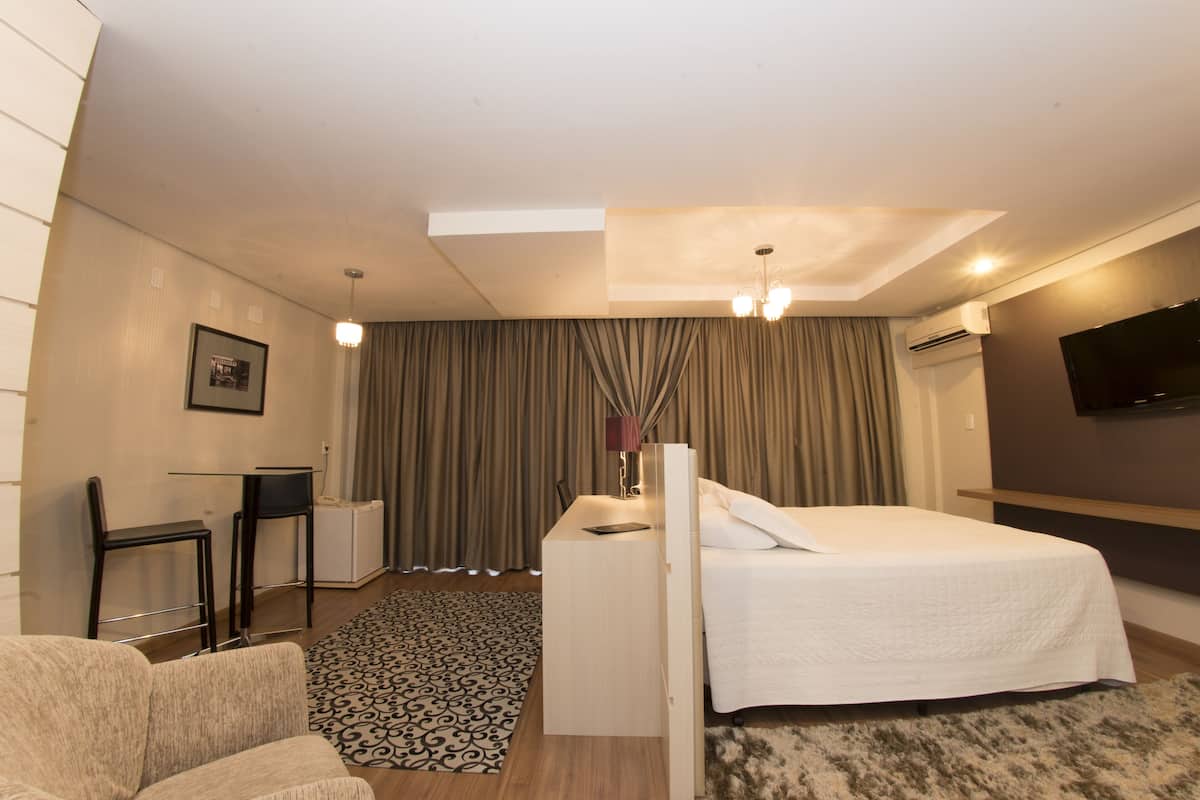Una habitación de hotel con una cama, un escritorio, una silla, un televisor y una alfombra estampada.