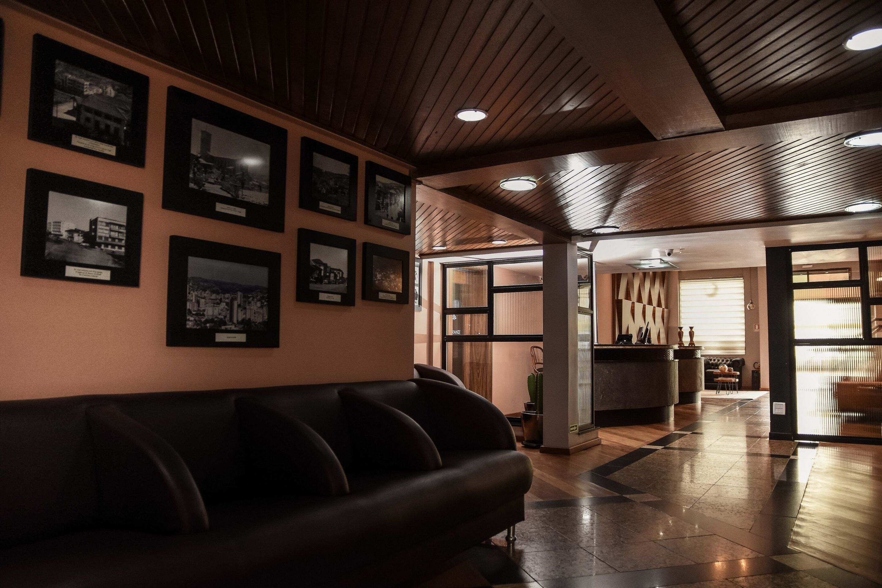 A lobby with a black leather sofa, framed photographs on the wall, and a wooden ceiling.