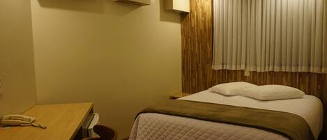 A hotel room with a bed, a desk, and a telephone.