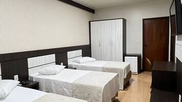A hotel room with three beds, a wooden floor, a large wardrobe, and a flat-screen TV.