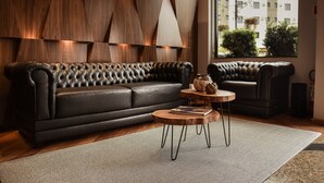 Un salon moderne avec un canapé en cuir, une table basse en bois et une grande fenêtre donnant sur des immeubles et des espaces verts.