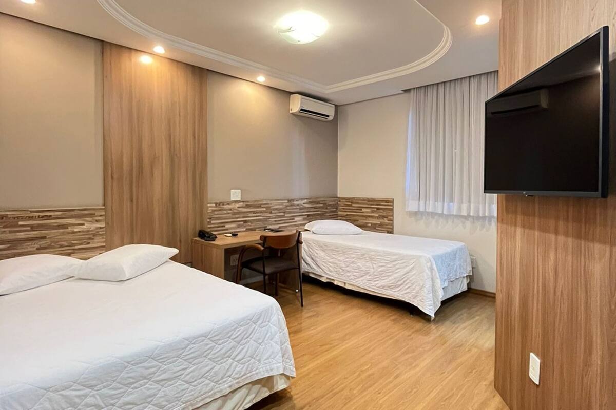 Habitación de hotel con dos camas, un escritorio, una silla, un televisor montado en la pared y un equipo de aire acondicionado.