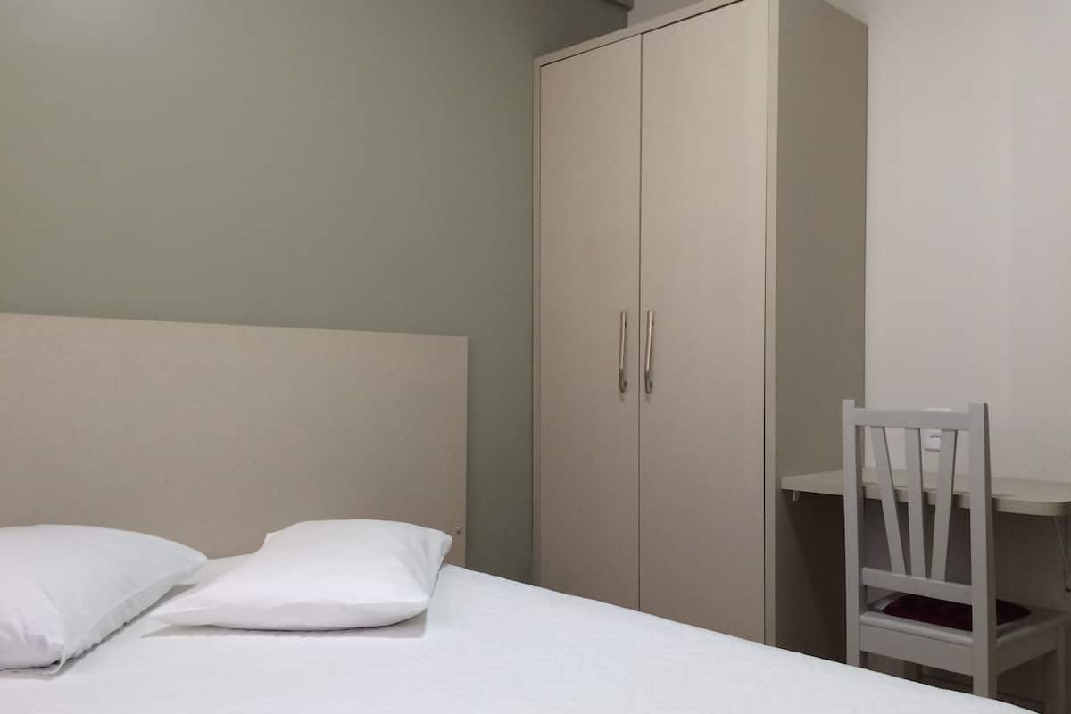 Un dormitorio con una cama, dos almohadas, un armario blanco y una silla blanca.