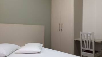 Un dormitorio con una cama, dos almohadas, un armario blanco y una silla blanca.