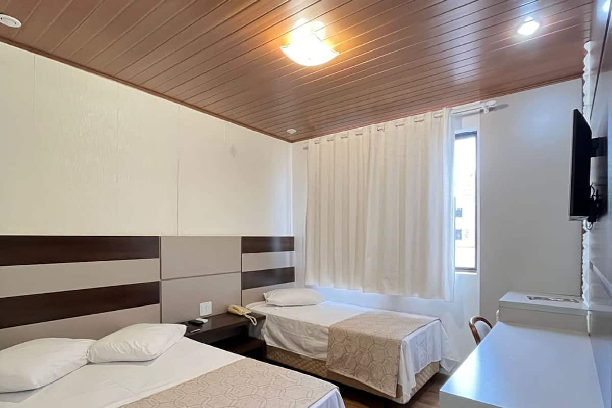 Una habitación de hotel con dos camas, un escritorio, un televisor y una ventana con cortinas.