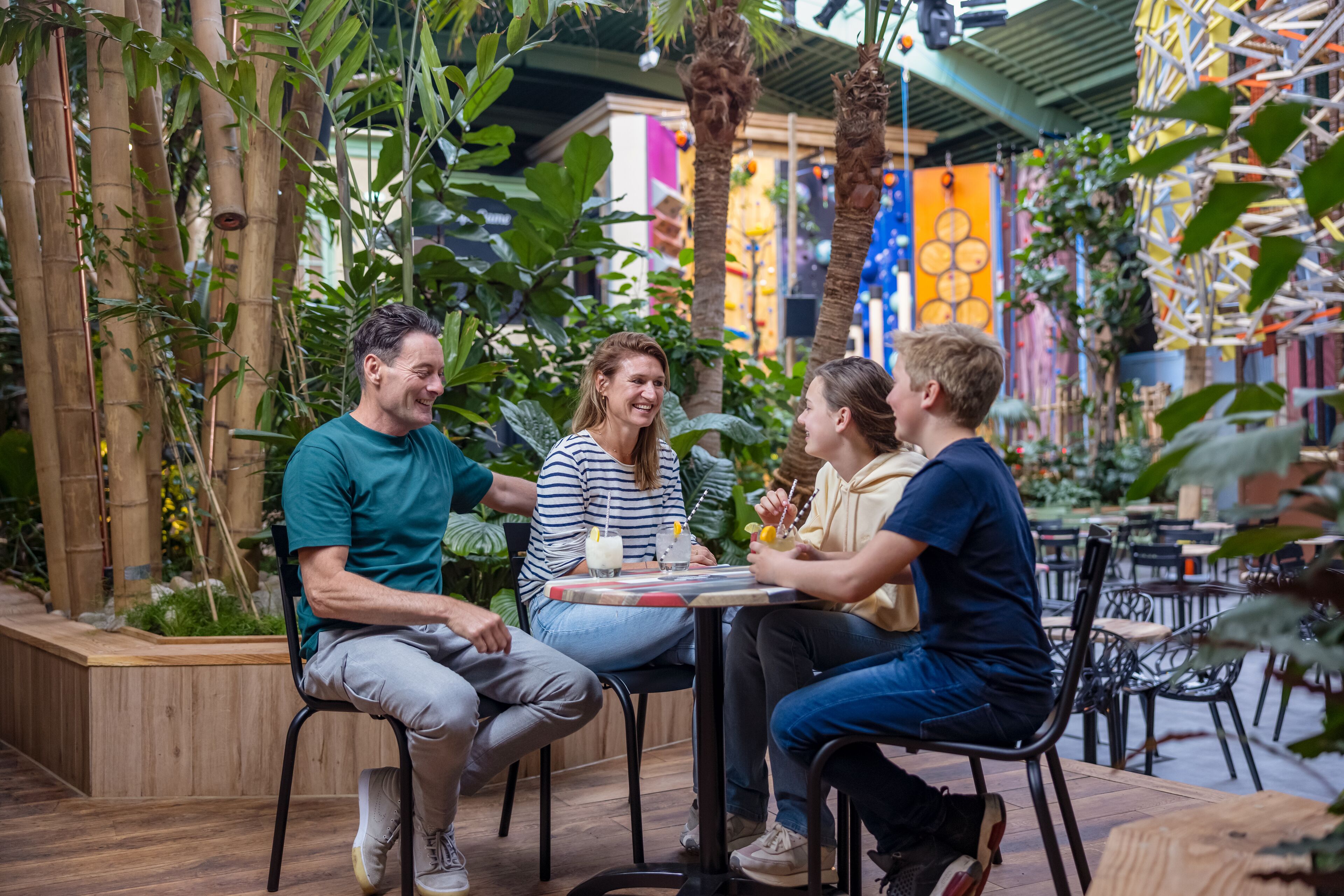 Eine Gruppe von Personen sitzt an einem Tisch in einer Gartenumgebung mit Bambuspflanzen und Holzmöbeln.