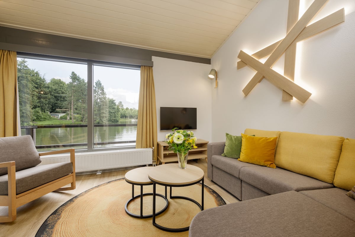 A modern living room with a sofa, two small tables, a TV, and a view of a lake.
