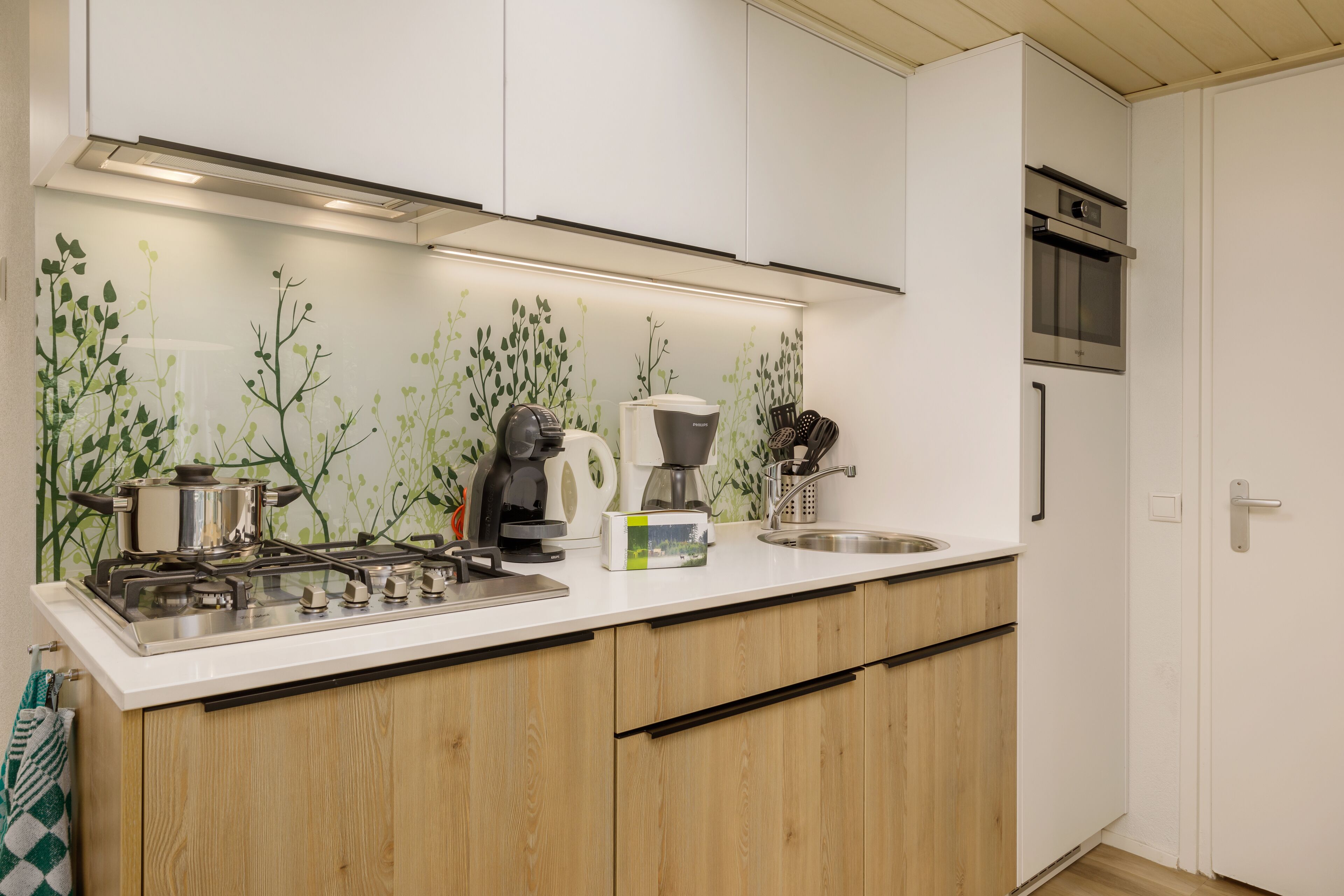 Eine moderne Küche mit weißen Schränken, einer Edelstahl-Arbeitsplatte, einem Gasherd, einer Kaffeemaschine und einer Mikrowelle.