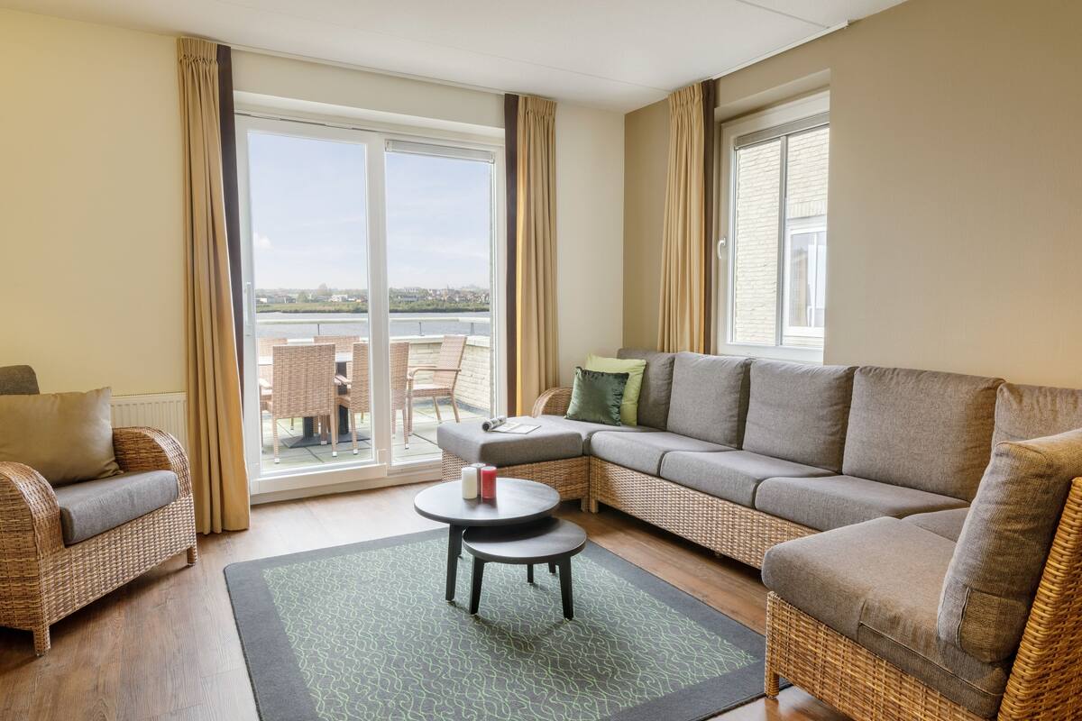 A modern living room with a sofa, a chair, a small table, and a view through a glass door to the outside.