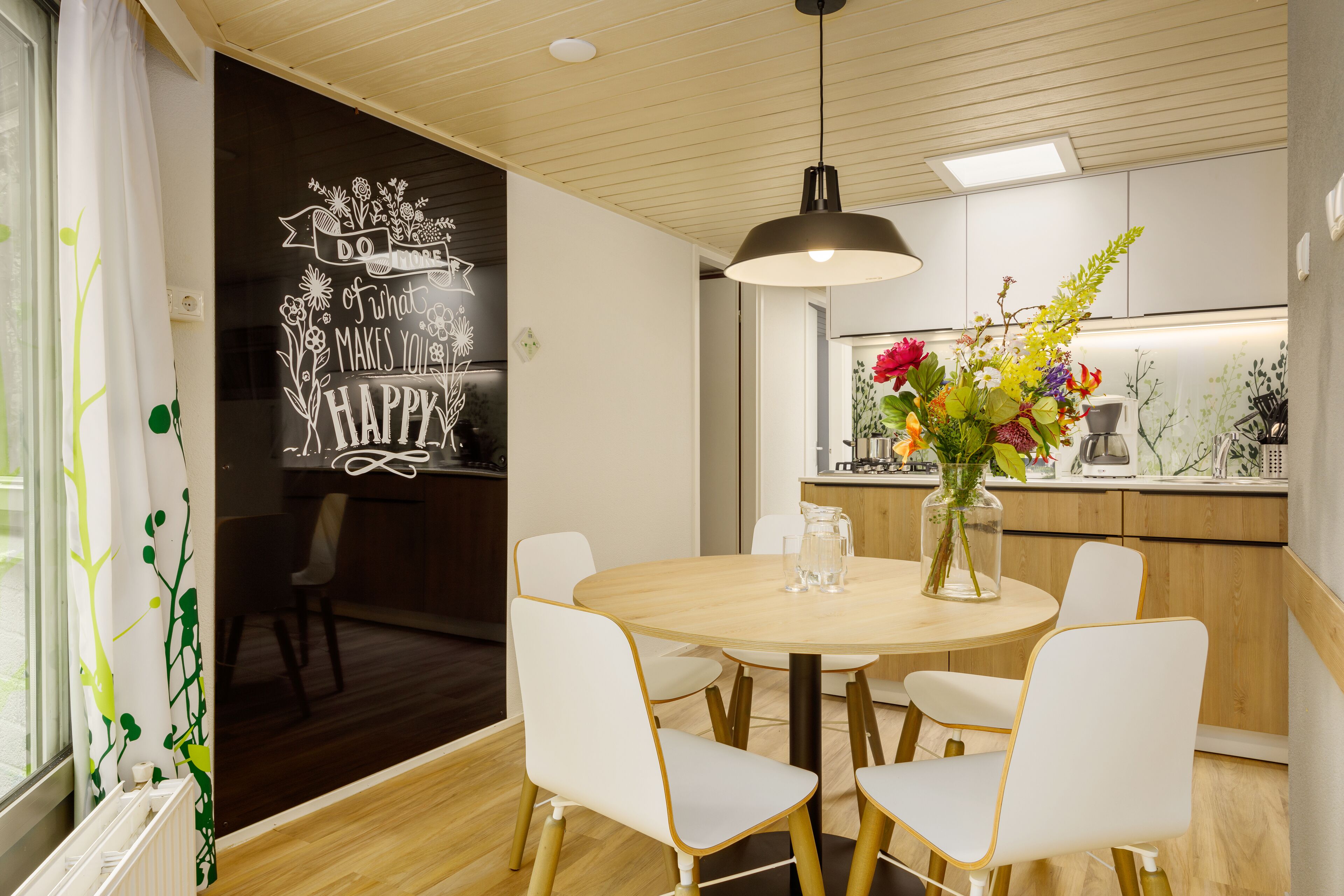 A modern dining area with a round table, white chairs, and a hanging pendant light.
