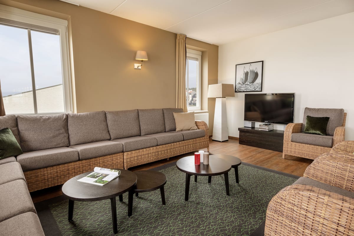 A modern living room with a sofa, two armchairs, a coffee table, a TV, and a lamp.