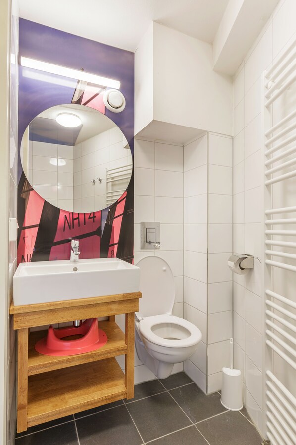 A bathroom with a white sink, a mirror, a toilet, and a shower area. - Center Parcs Port Zélande (Ouddorp)