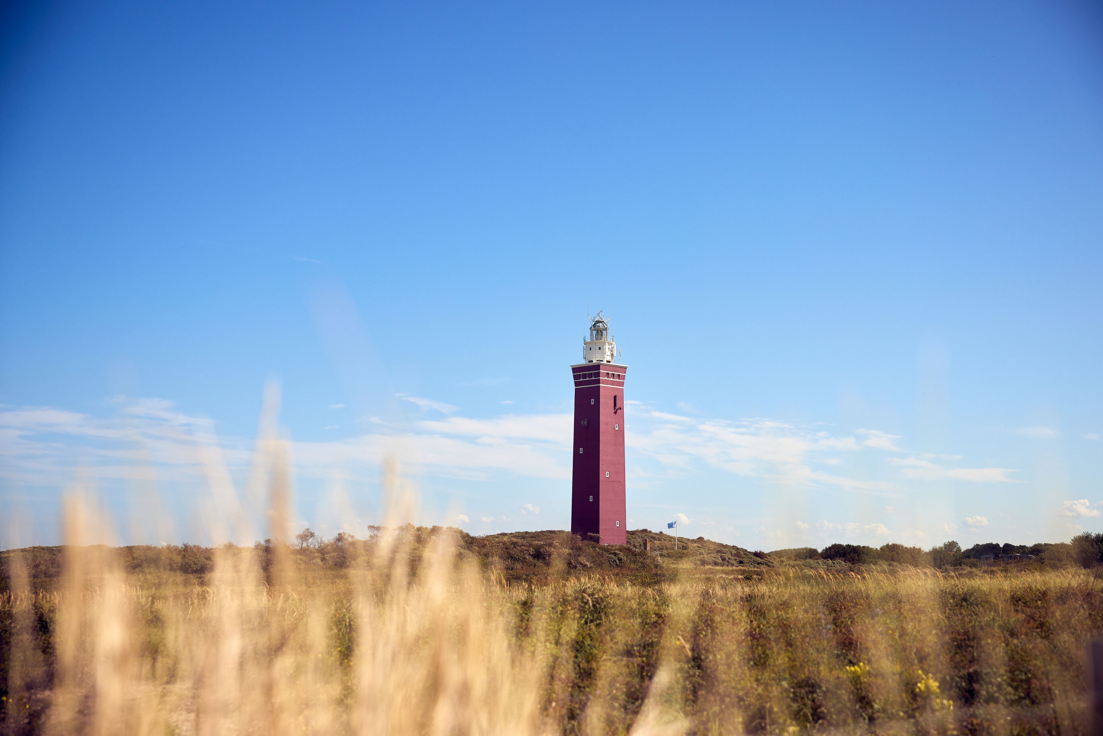 Ein Leuchtturm auf einem Hügel vor blauem Himmel.