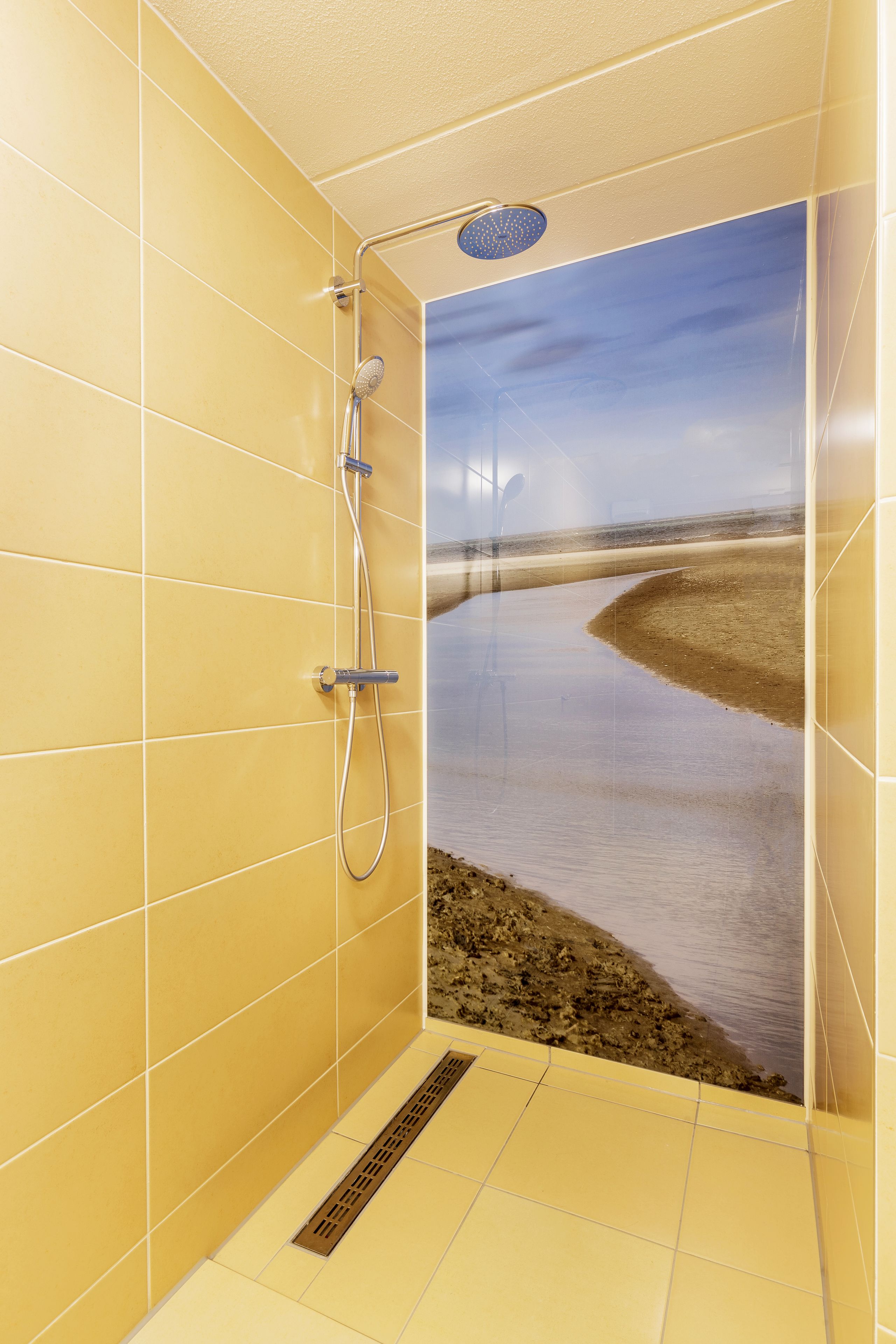 Ein Badezimmer mit gelben Fliesen, einer Dusche und einem großen Poster mit einer Strandansicht.