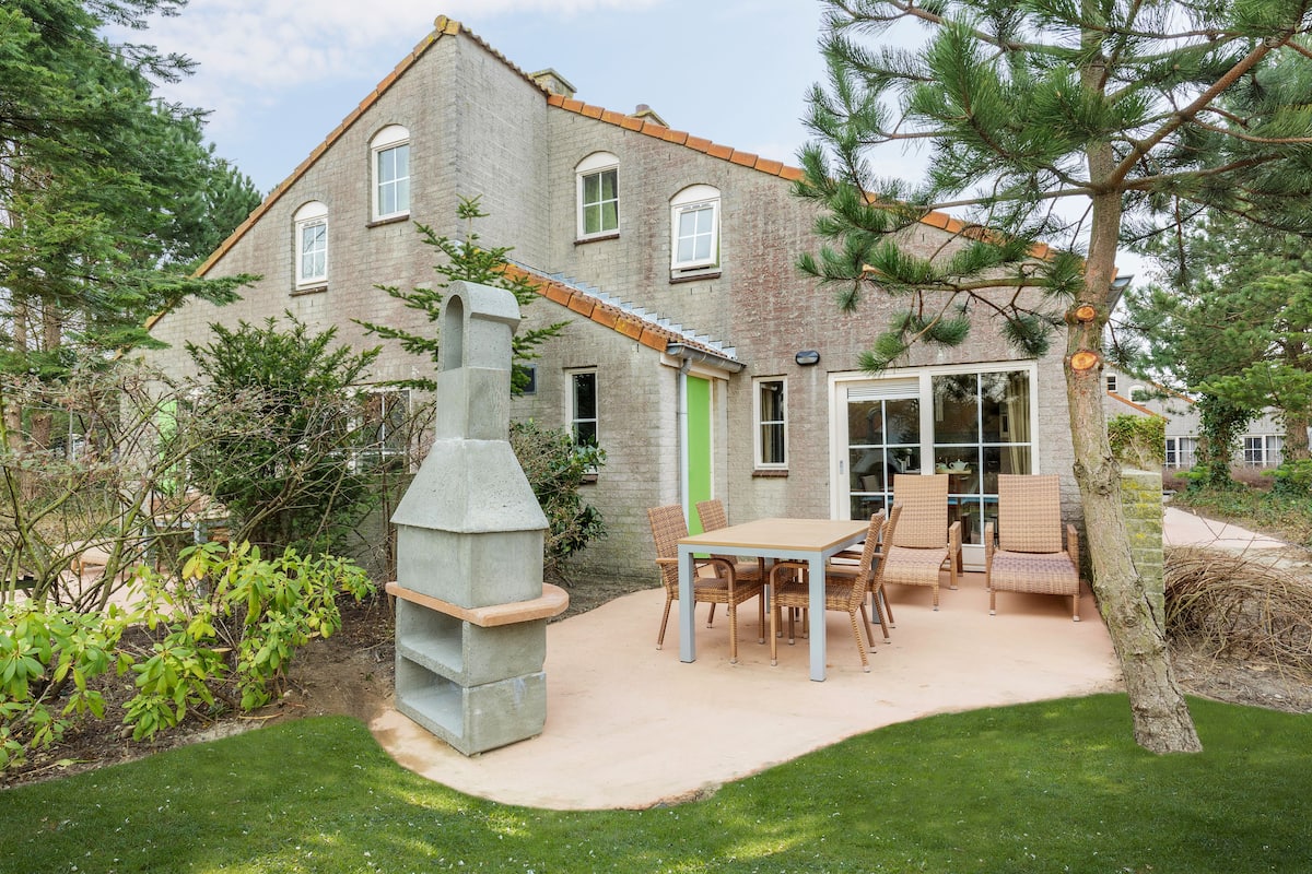 Una casa de dos pisos con fachada de piedra, una puerta verde y un patio con mesa y sillas.