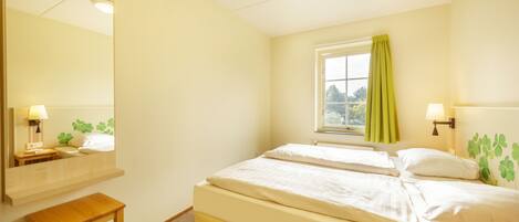 A bedroom with two beds, a window with curtains, a bedside table, and a mirror.