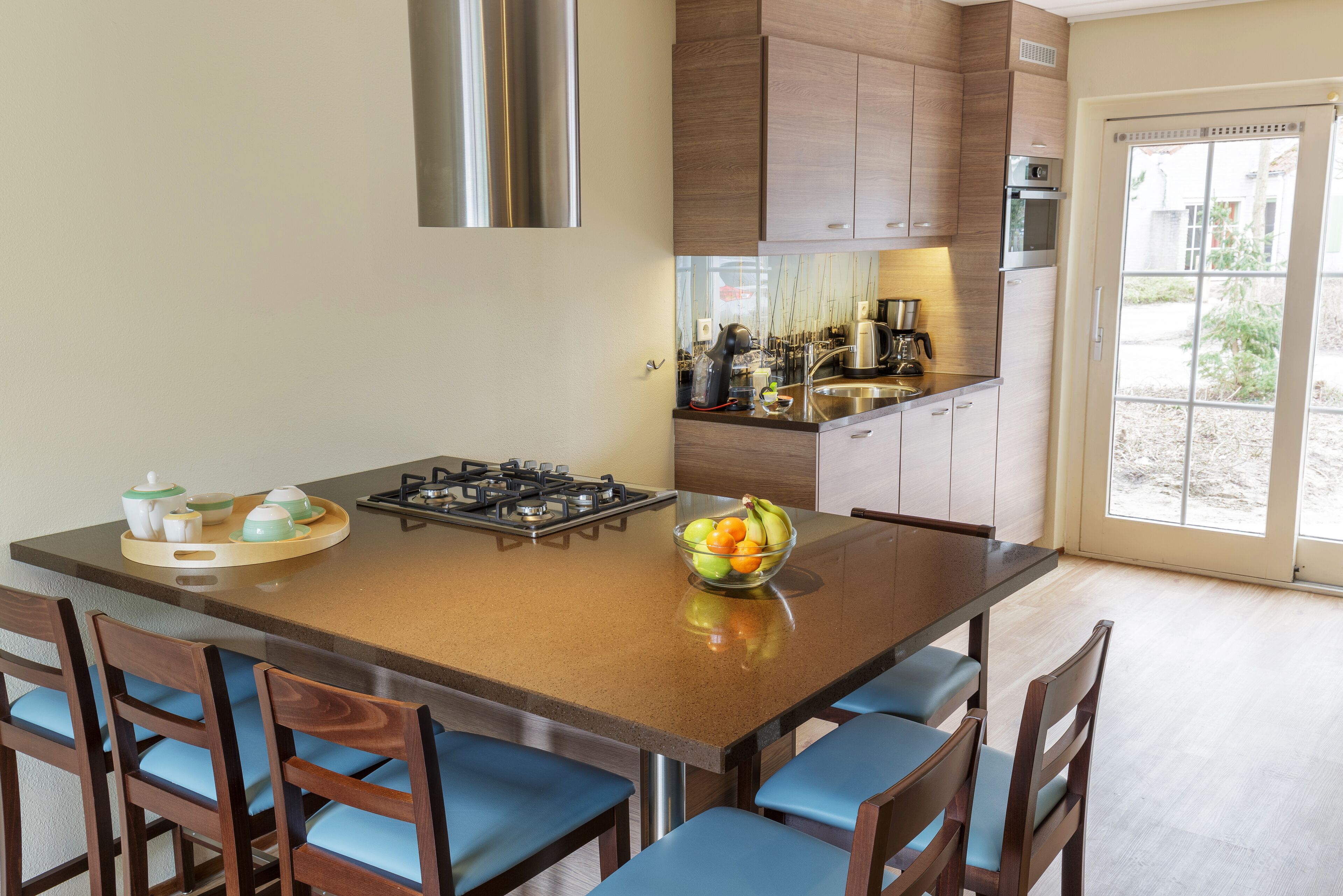 A modern kitchen with a central island, wooden cabinets, and a large window.