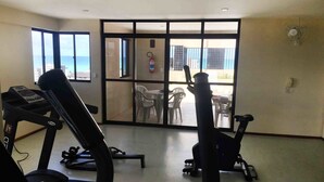 Un gimnasio con cintas de correr y bicicletas estáticas, un extintor de incendios y vistas al exterior a través de grandes puertas de vidrio.