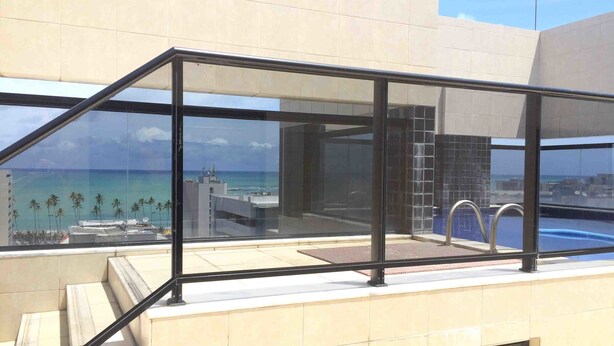 Un balcón con paredes de vidrio que ofrece vistas al océano y a una piscina.