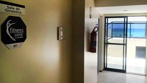 Un letrero de gimnasio, un extintor y una puerta de cristal que da a un balcón con vista al océano.