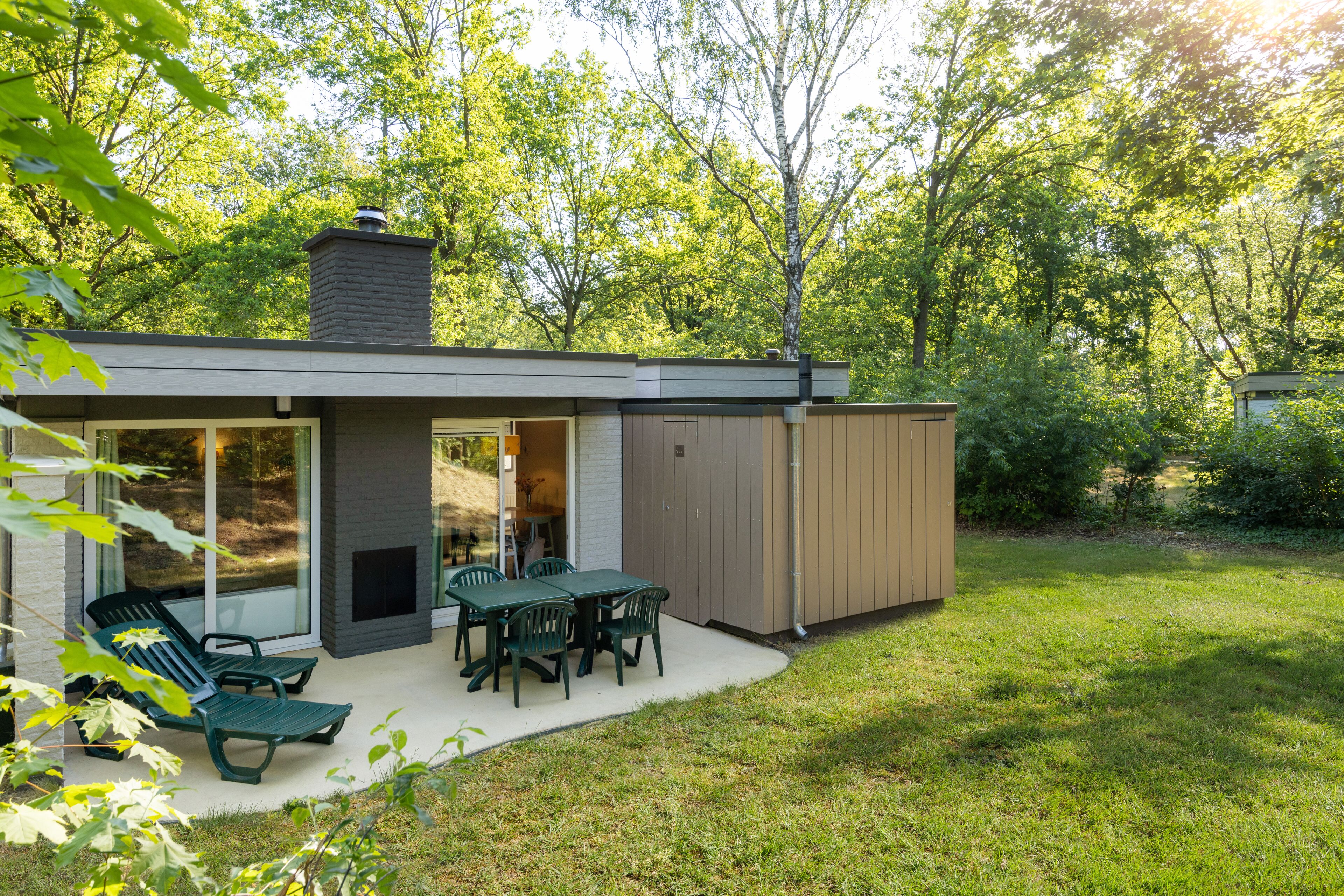 A modern house with a patio, outdoor seating, and a large window overlooking a garden.