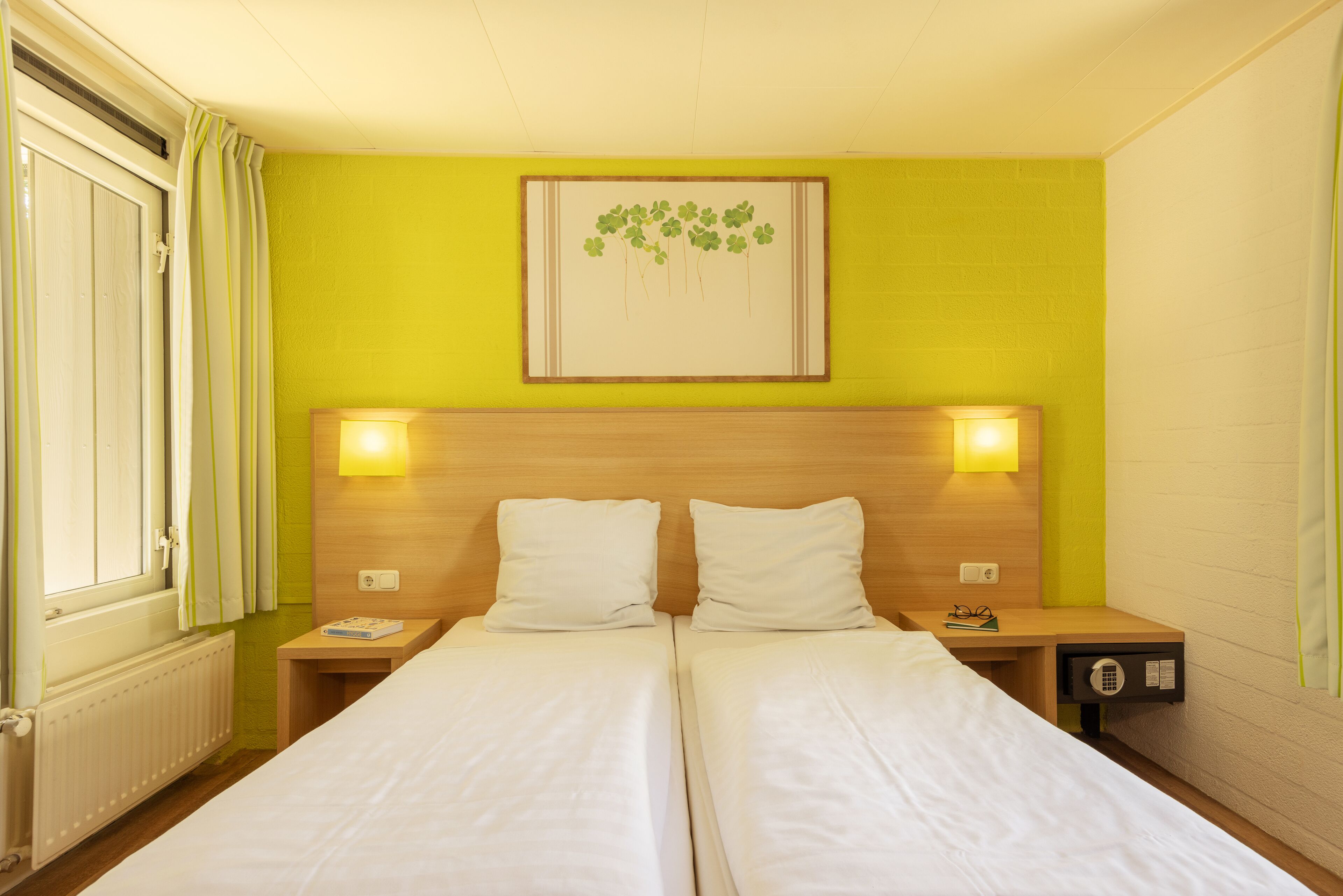 A double bed room with two bedside tables, a headboard with a framed artwork, and a window with curtains.