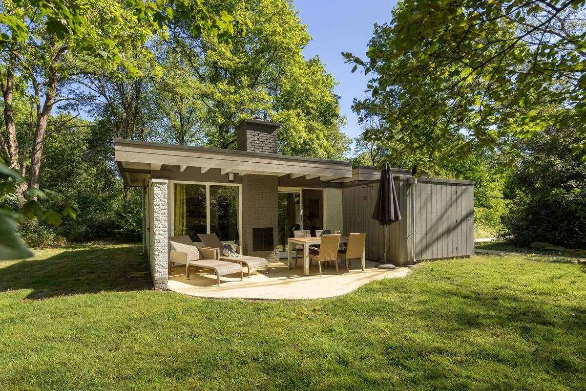 A small, single-story house with a patio area, a stone fireplace, and a covered outdoor seating area.
