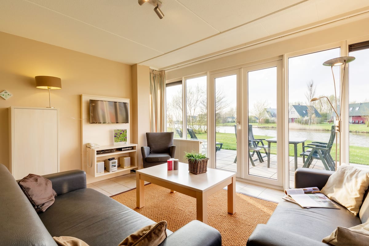 A spacious living room with a sofa set, a coffee table, and a television mounted on the wall.