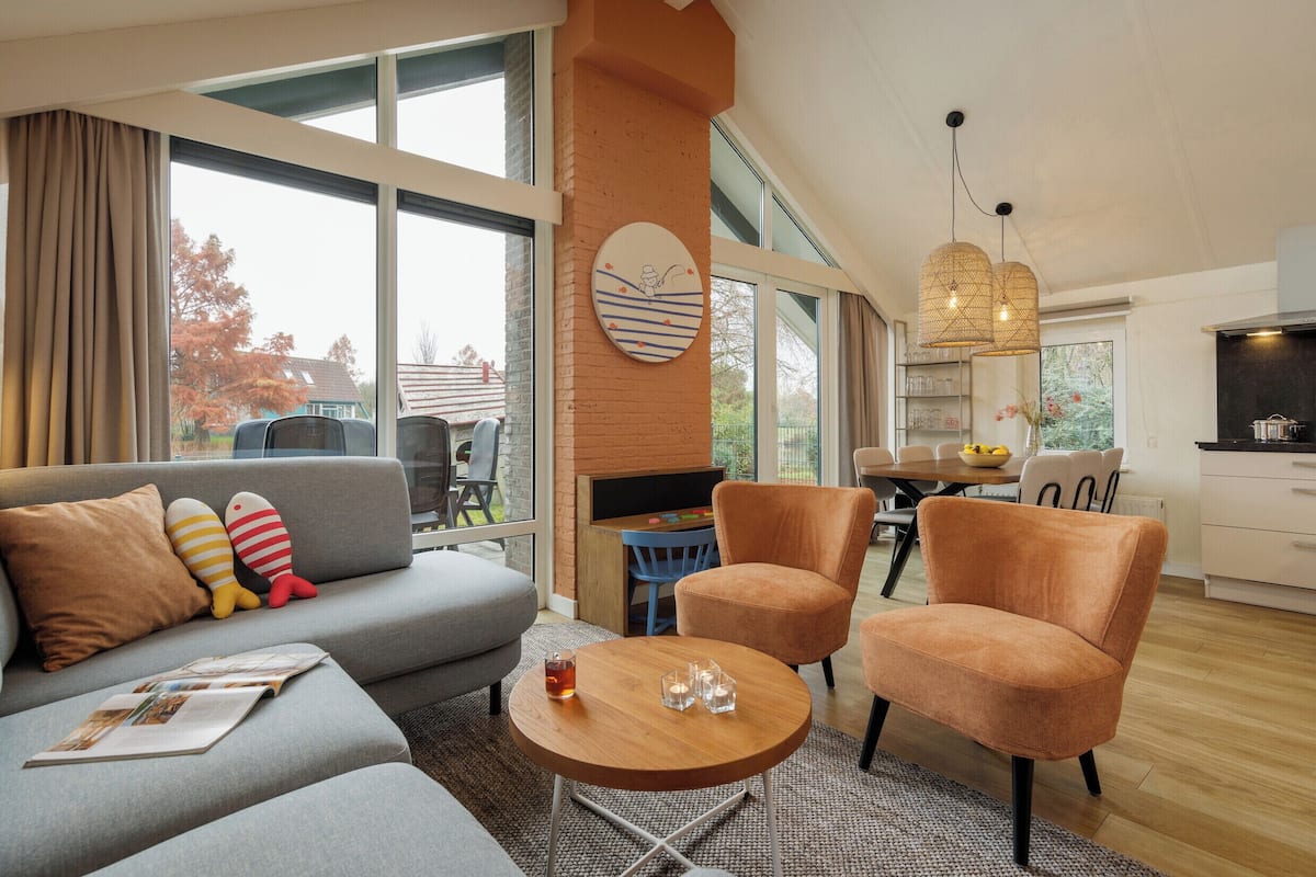 A modern living room with a grey sofa, orange armchairs, a wooden coffee table, and a fireplace.