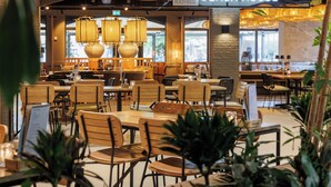 A restaurant interior with wooden tables and chairs, hanging pendant lights, and a sign reading "BEACH HOUSE". - Center Parcs Parc Sandur (Emmen)