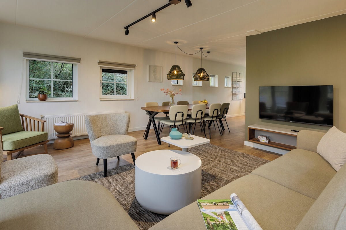 A modern living room with a sofa, armchairs, a coffee table, and a dining area with chairs and a table.